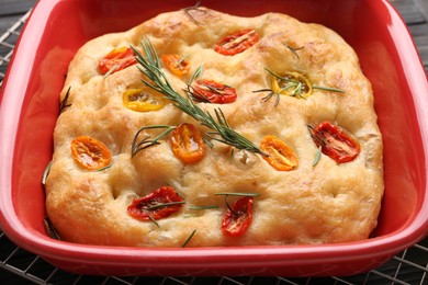 Photo of Delicious focaccia with tomatoes and rosemary in baking dish on table, closeup