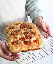 Photo of Woman holding delicious focaccia with tomatoes and spices on light background, closeup