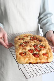 Photo of Woman holding delicious focaccia with tomatoes and spices on light background, closeup