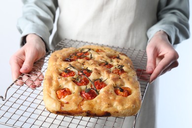 Photo of Woman holding delicious focaccia with tomatoes and spices on light background, closeup