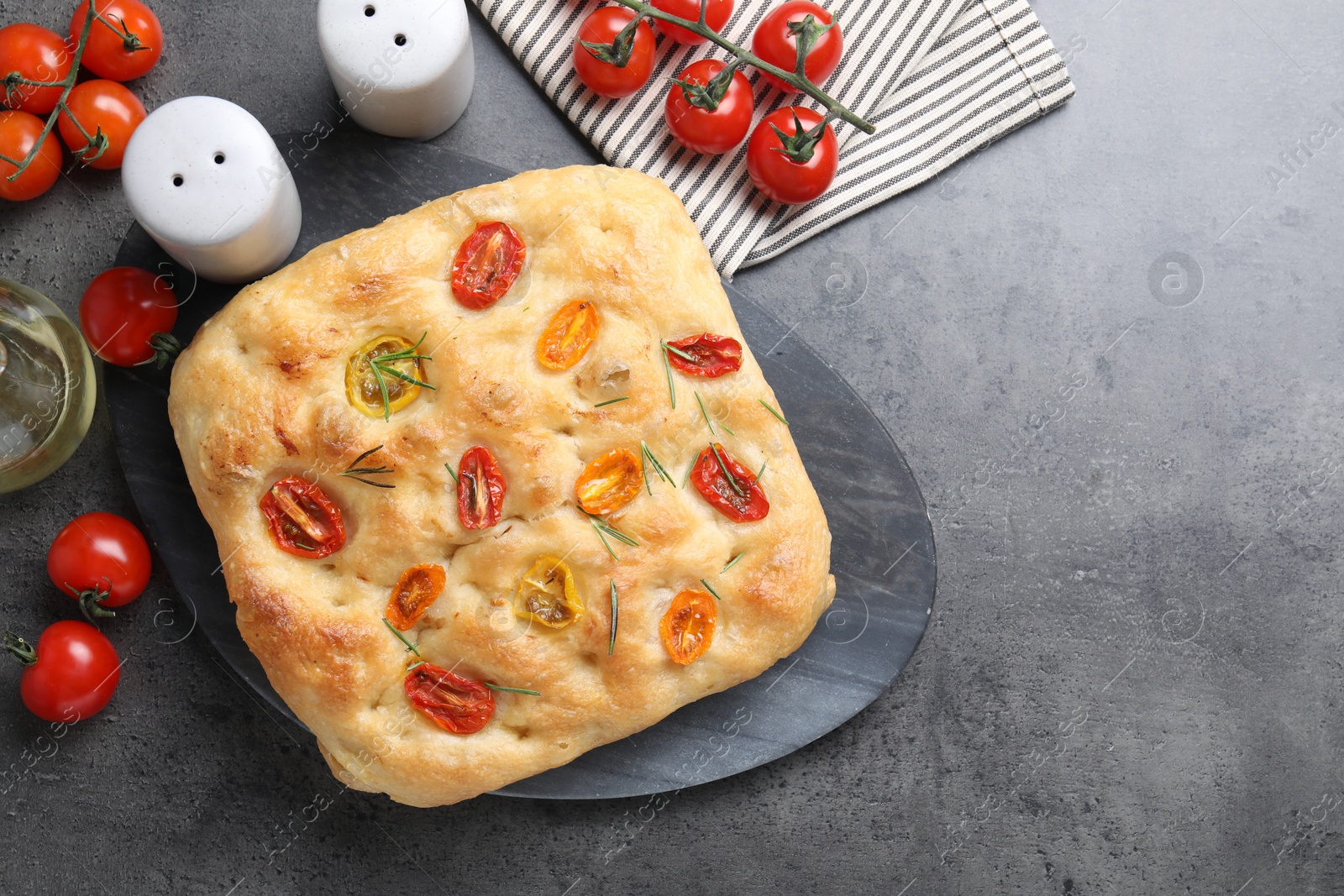 Delicious focaccia with tomatoes, spices and oil on gray textured table, flat lay. Space for text Photo of Delicious focaccia with tomatoes, spices and oil on gray textured table, flat lay. Space for text