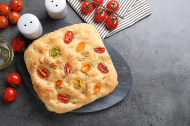 Photo of Delicious focaccia with tomatoes, spices and oil on gray textured table, flat lay. Space for text