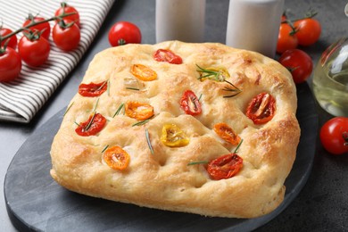 Photo of Delicious focaccia with tomatoes and rosemary on gray table, closeup