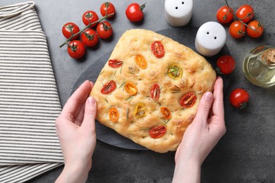 Photo of Woman with delicious focaccia with tomatoes, spices and oil at gray textured table, top view