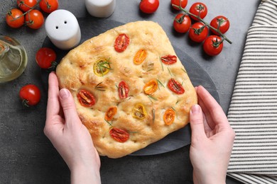Photo of Woman with delicious focaccia with tomatoes, spices and oil at gray textured table, top view
