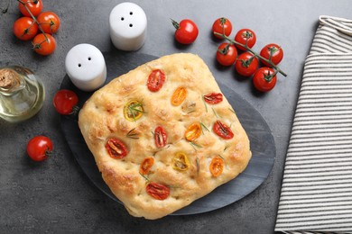 Photo of Delicious focaccia with tomatoes, spices and oil on gray textured table, flat lay
