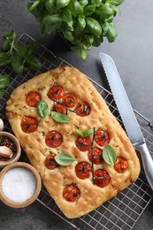 Photo of Delicious focaccia with tomatoes, spices and knife on gray table, flat lay