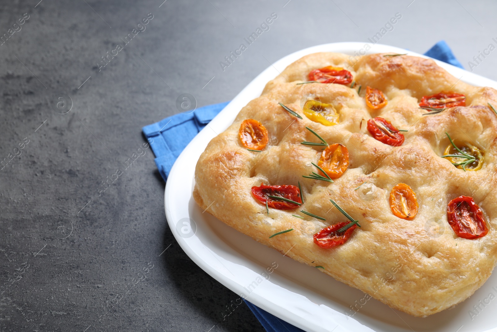 Delicious focaccia with tomatoes and rosemary on gray textured table, closeup. Space for text Photo of Delicious focaccia with tomatoes and rosemary on gray textured table, closeup. Space for text