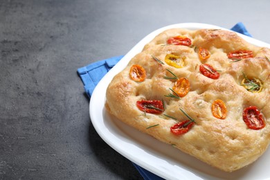 Photo of Delicious focaccia with tomatoes and rosemary on gray textured table, closeup. Space for text