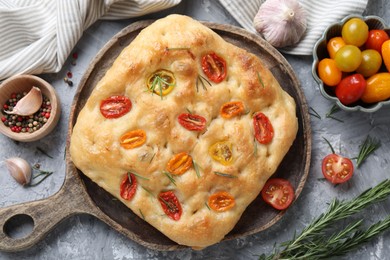Photo of Delicious focaccia with tomatoes and spices on gray textured table, flat lay