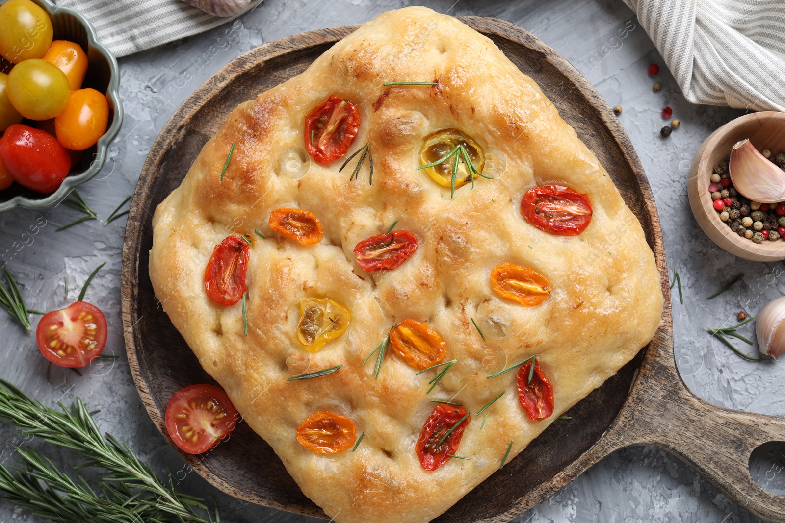 Delicious focaccia with tomatoes and spices on gray textured table, flat lay Photo of Delicious focaccia with tomatoes and spices on gray textured table, flat lay