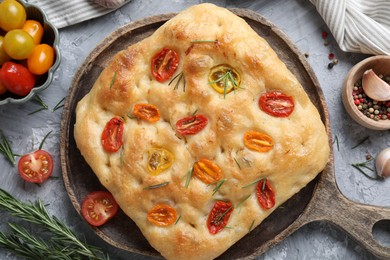 Photo of Delicious focaccia with tomatoes and spices on gray textured table, flat lay