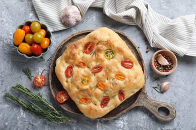 Photo of Delicious focaccia with tomatoes and spices on gray textured table, flat lay