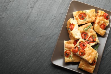 Photo of Pieces of delicious focaccia with tomatoes and spices on gray textured table, top view. Space for text