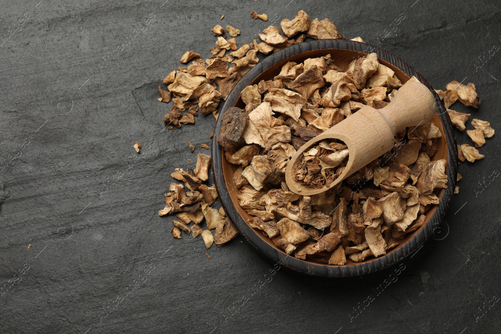 Pieces of dry chicory roots in bowl and scoop on dark textured table, top view. Space for text Photo of Pieces of dry chicory roots in bowl and scoop on dark textured table, top view. Space for text