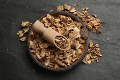 Photo of Pieces of dry chicory roots in bowl and scoop on dark textured table, top view