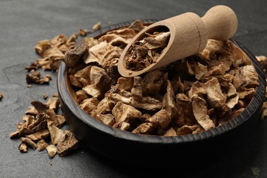 Photo of Pieces of dry chicory roots in bowl and scoop on dark textured table, closeup
