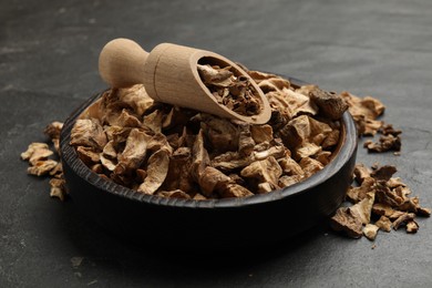 Photo of Pieces of dry chicory roots in bowl and scoop on dark textured table, closeup