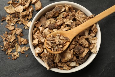 Photo of Pieces of dry chicory roots in bowl and spoon on dark textured table, top view