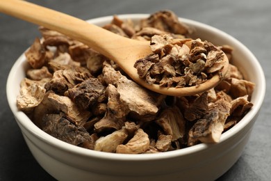 Photo of Pieces of dry chicory roots in bowl and spoon on dark table, closeup