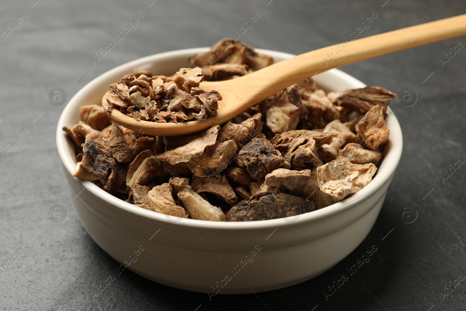 Pieces of dry chicory roots in bowl and spoon on dark table, closeup Photo of Pieces of dry chicory roots in bowl and spoon on dark table, closeup