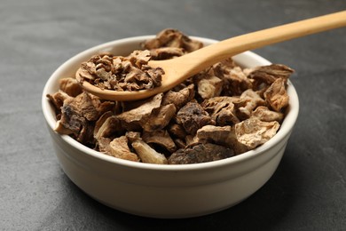 Photo of Pieces of dry chicory roots in bowl and spoon on dark table, closeup