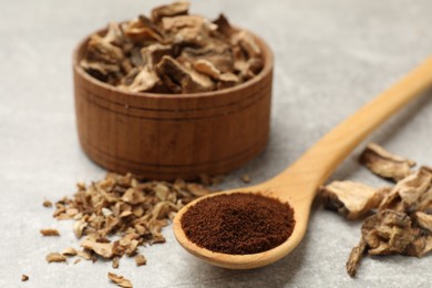 Photo of Pieces of dry chicory roots in bowl and spoon with powder on gray textured table, closeup