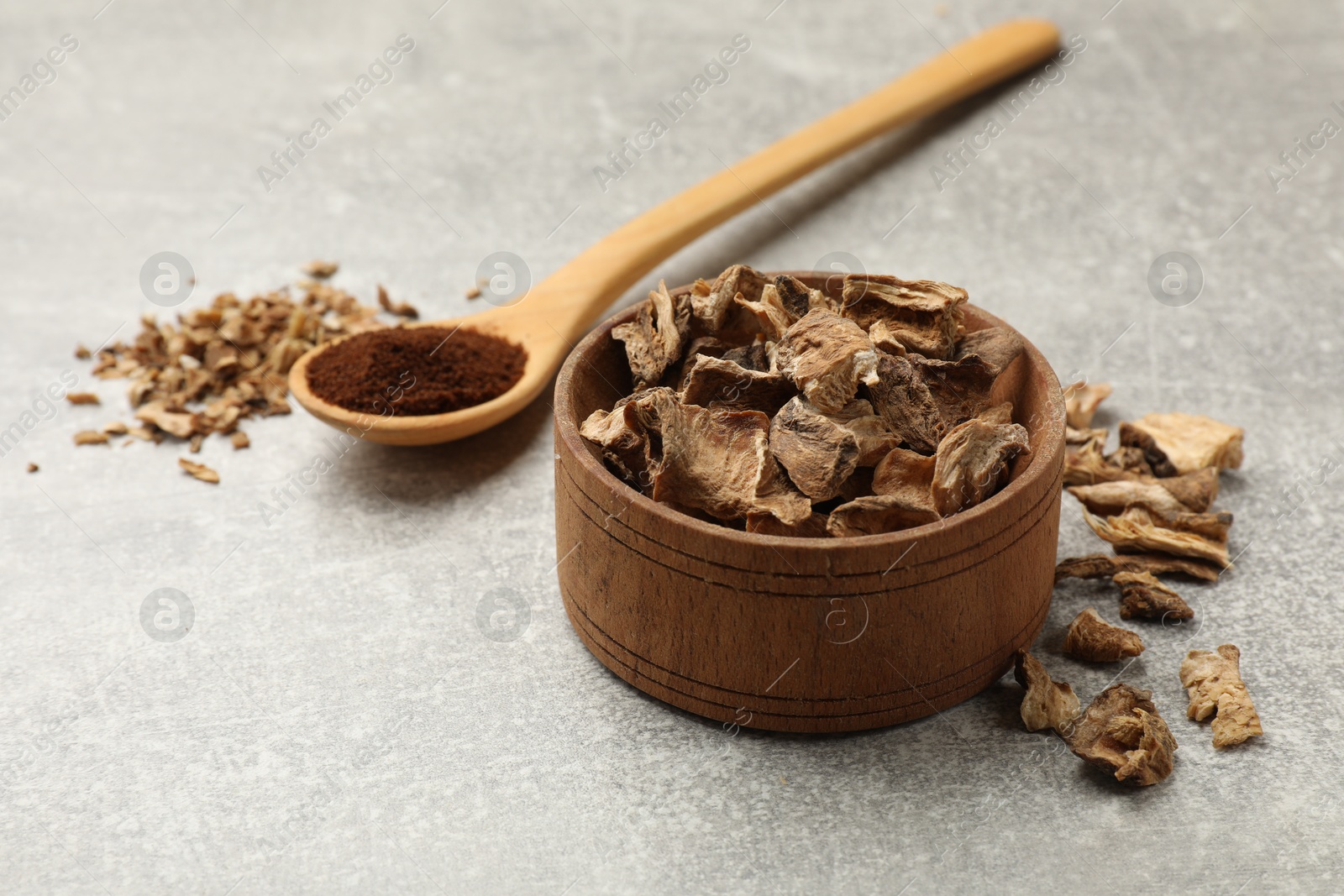 Pieces of dry chicory roots in bowl and spoon with powder on gray textured table Photo of Pieces of dry chicory roots in bowl and spoon with powder on gray textured table