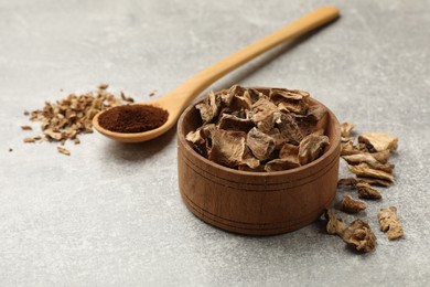 Photo of Pieces of dry chicory roots in bowl and spoon with powder on gray textured table