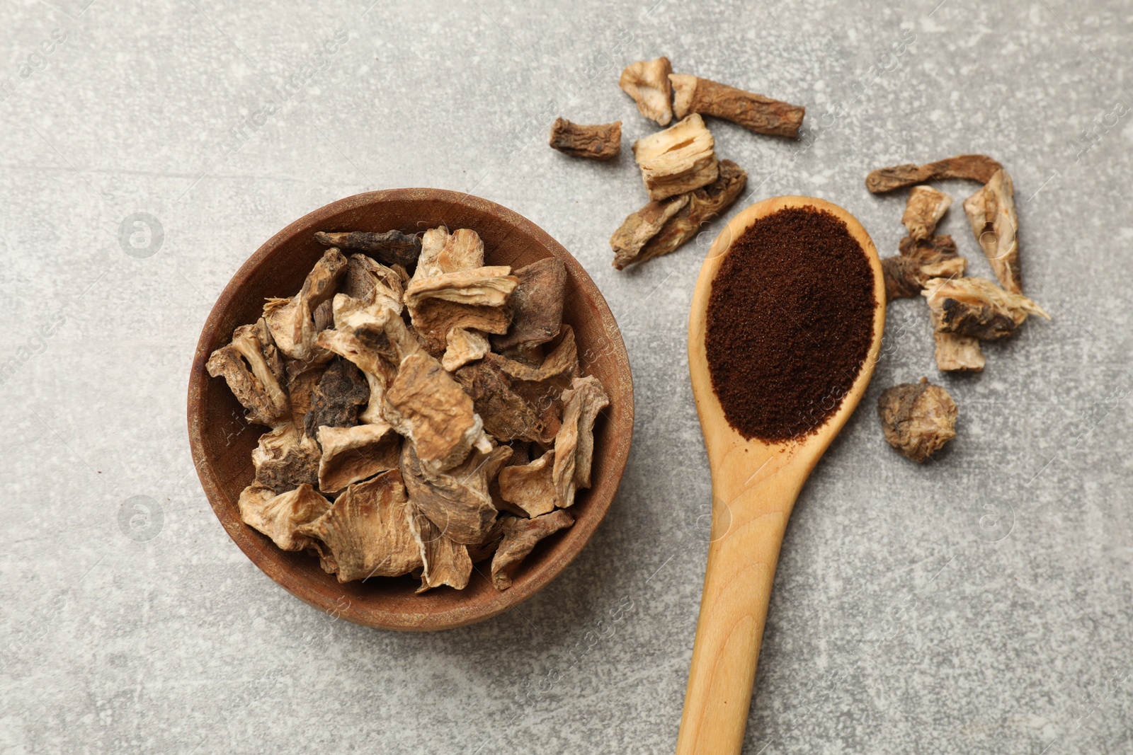 Pieces of dry chicory roots in bowl and spoon with powder on gray textured table, flat lay Photo of Pieces of dry chicory roots in bowl and spoon with powder on gray textured table, flat lay