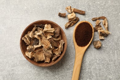 Photo of Pieces of dry chicory roots in bowl and spoon with powder on gray textured table, flat lay