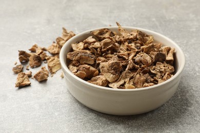 Photo of Pieces of dry chicory roots in bowl on gray textured table, closeup