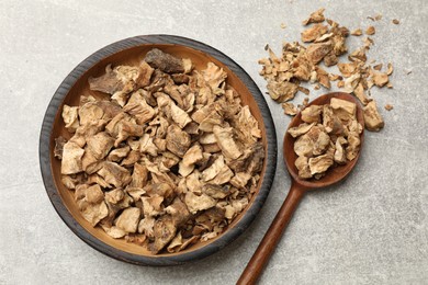 Photo of Pieces of dry chicory roots in bowl and spoon on gray textured table, flat lay