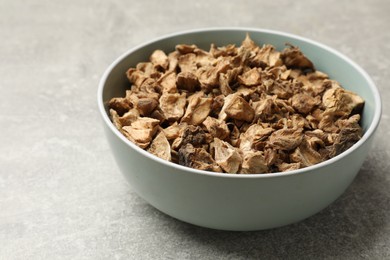 Photo of Pieces of dry chicory roots in bowl on gray textured table, closeup