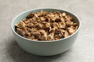 Photo of Pieces of dry chicory roots in bowl on gray textured table, closeup