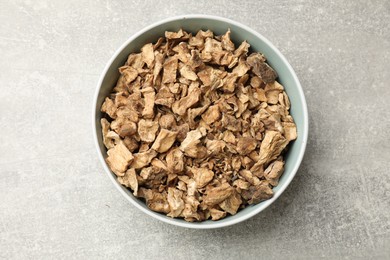 Photo of Pieces of dry chicory roots in bowl on gray textured table, top view