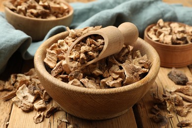 Photo of Pieces of dry chicory roots in bowls and scoop on wooden table, closeup