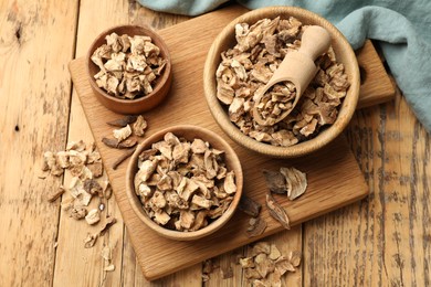 Photo of Pieces of dry chicory roots in bowls and scoop on wooden table, top view
