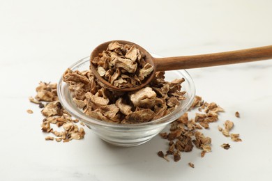 Photo of Pieces of dry chicory roots in bowl and spoon on white table, closeup
