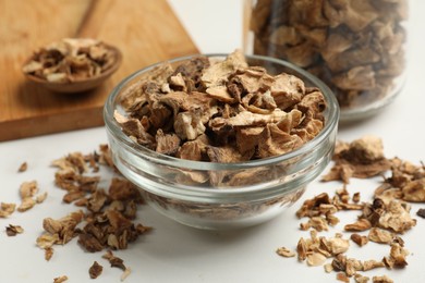 Photo of Pieces of dry chicory roots in bowl, jar and spoon on white table, closeup