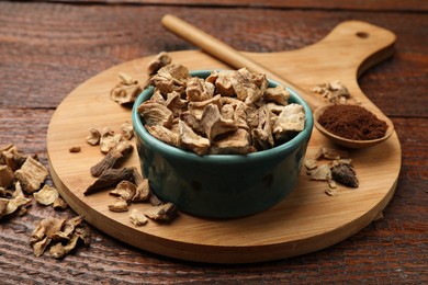 Photo of Pieces of dry chicory roots in bowl and spoon with powder on wooden table, closeup