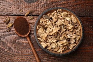 Photo of Pieces of dry chicory roots in bowl and spoon with powder on wooden table, flat lay