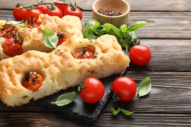 Photo of Pieces of delicious focaccia with tomatoes and spices on wooden table, closeup