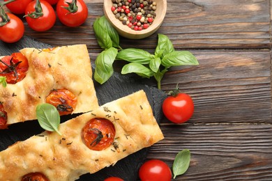 Photo of Pieces of delicious focaccia with tomatoes and spices on wooden table, flat lay