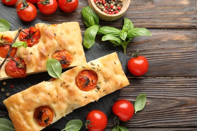 Photo of Pieces of delicious focaccia with tomatoes and spices on wooden table, flat lay