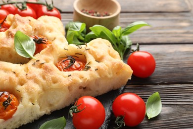 Photo of Pieces of delicious focaccia with tomatoes and spices on wooden table, closeup