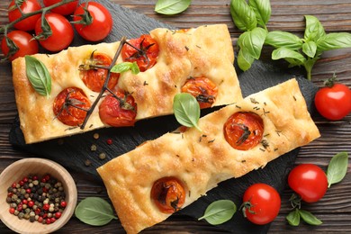 Photo of Pieces of delicious focaccia with tomatoes and spices on wooden table, flat lay