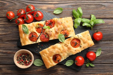 Photo of Pieces of delicious focaccia with tomatoes and spices on wooden table, flat lay