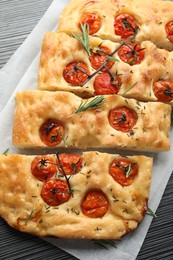 Photo of Cut delicious focaccia with tomatoes and spices on dark wooden table, top view