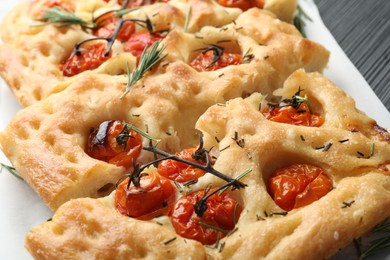 Photo of Cut delicious focaccia with tomatoes and spices on table, closeup
